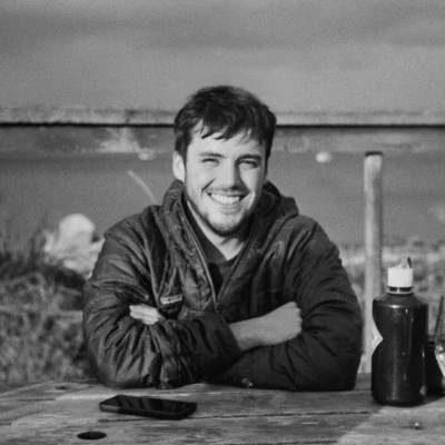 Marco Salguero smiling at an outdoor table, arms crossed, in a black-and-white photo.